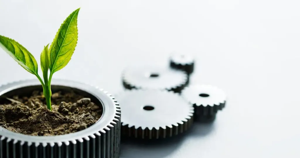 Plant seedling growing in soil inside a metal gear, with other gears in the background